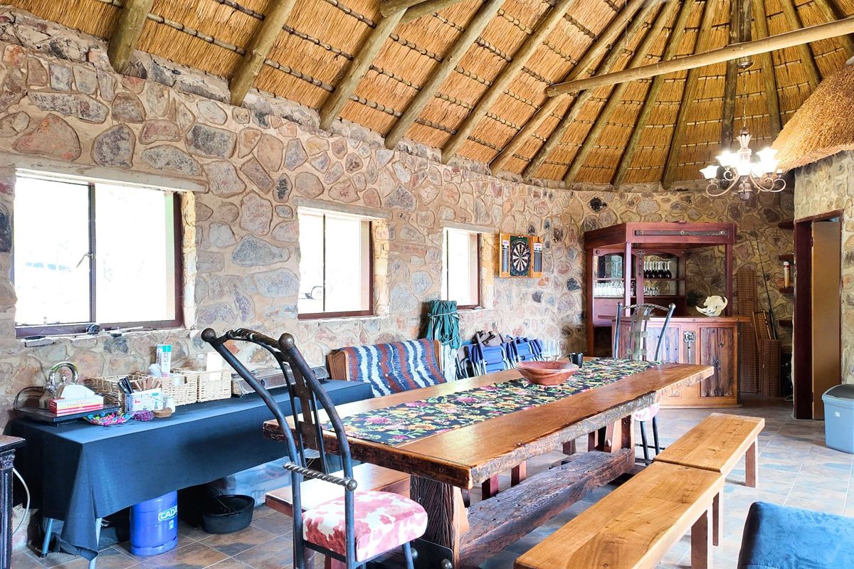Spacious living area featuring rustic stone walls, a traditional thatched roof with exposed timber rafters, and a built-in bar area.