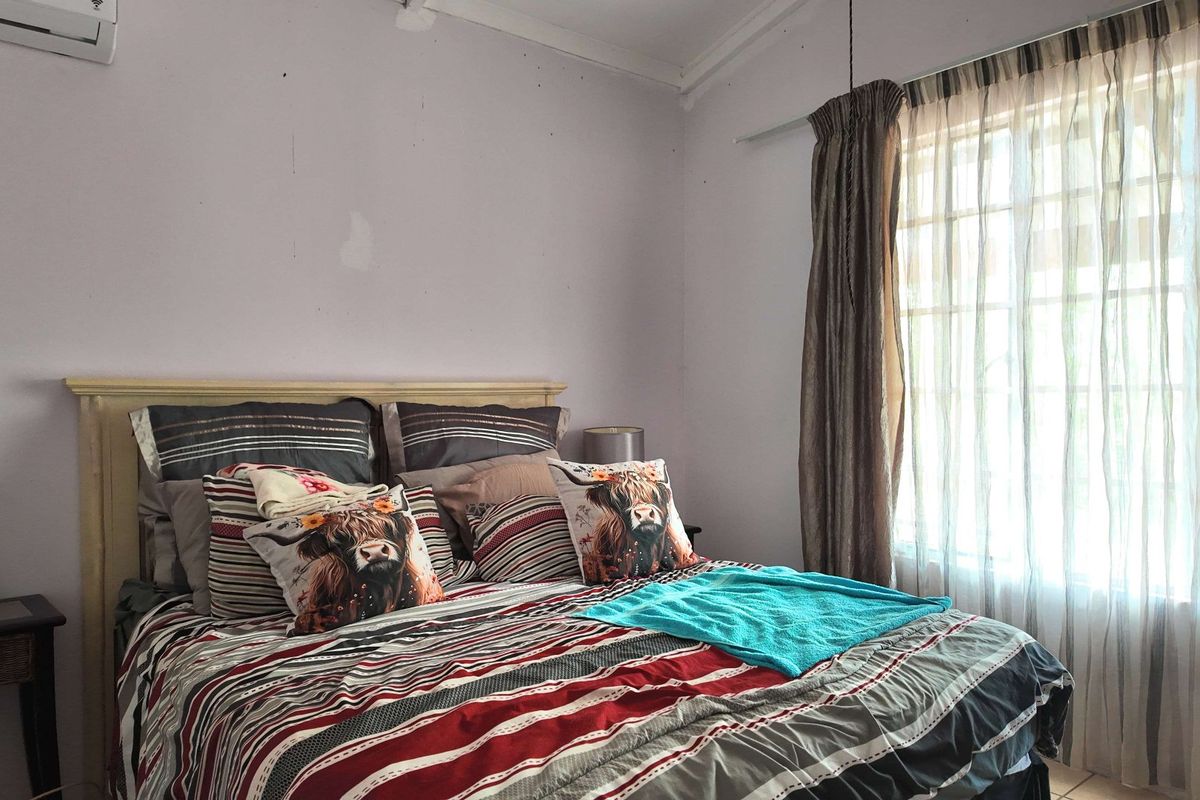 A bedroom featuring a window with curtain rails and a wall-mounted air conditioning unit.