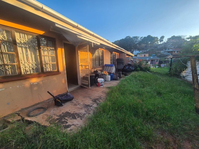 Rear exterior view of the apartment featuring a concrete patio, security gate, and metal window frames, requiring maintenance and landscaping improvements.