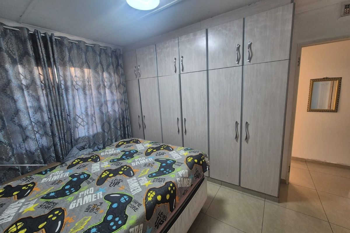 A well-maintained bedroom featuring extensive built-in cupboards, neutral tiled flooring, and a functional ceiling light fixture.