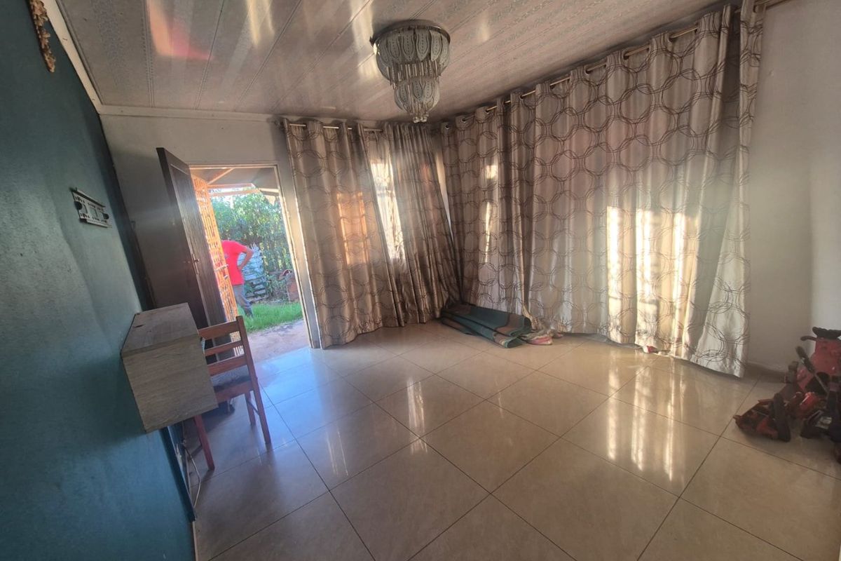 A spacious living area featuring tiled flooring and a central ceiling light fixture, with direct access to an outdoor space.