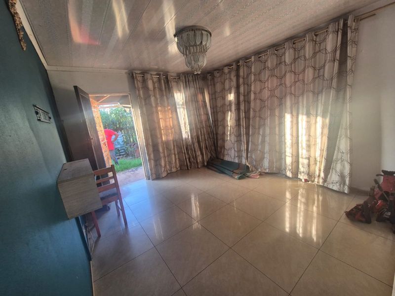A spacious living area featuring tiled flooring and a central ceiling light fixture, with direct access to an outdoor space.