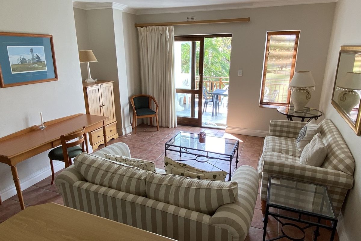 A comfortable living room featuring terracotta floor tiles, crown molding, and a sliding glass door providing access to an outdoor patio area.