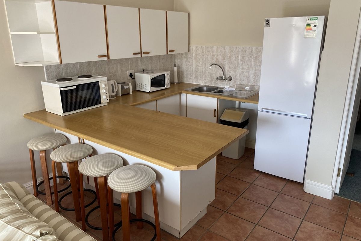 A compact kitchen featuring laminate countertops, white cabinetry, tiled backsplash, and tiled flooring, providing a functional and practical cooking and preparation space.