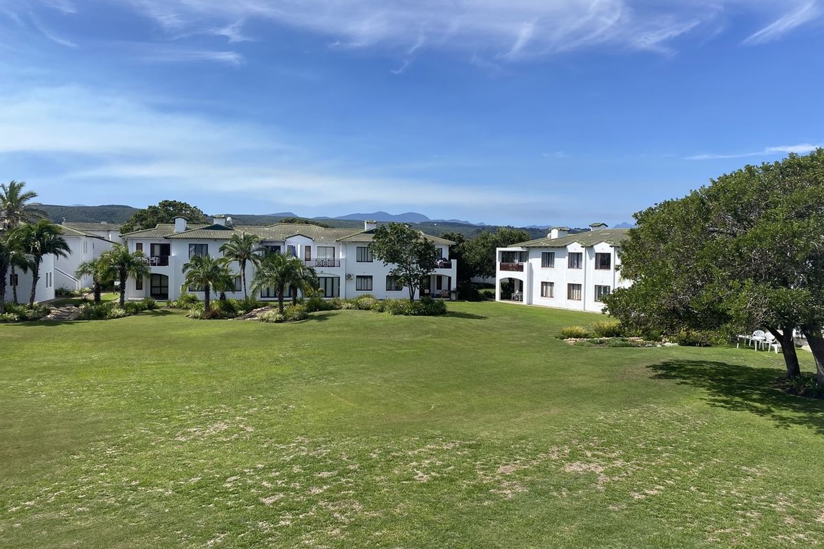 A view of the rear exterior of the apartment complex, featuring well-maintained lawns, landscaped gardens, and multi-story residential buildings with balconies.