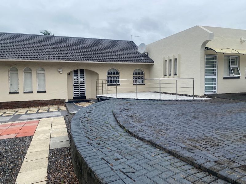 Front exterior view of the property featuring a paved driveway, raised patio area with stainless steel balustrade, and arched window detailing.