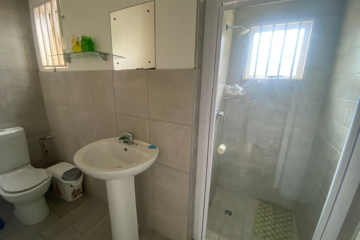 A functional bathroom featuring a pedestal basin, toilet, and a glass-enclosed shower with neutral wall and floor tiling.