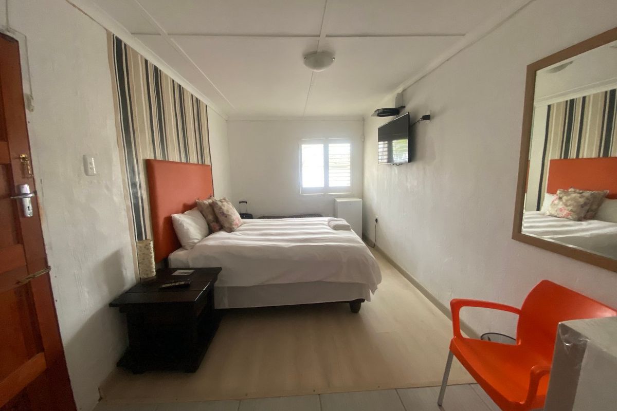 A functional bedroom featuring laminate flooring, a wall-mounted television, and a window with louvre shutters, offering a simple and practical living space.