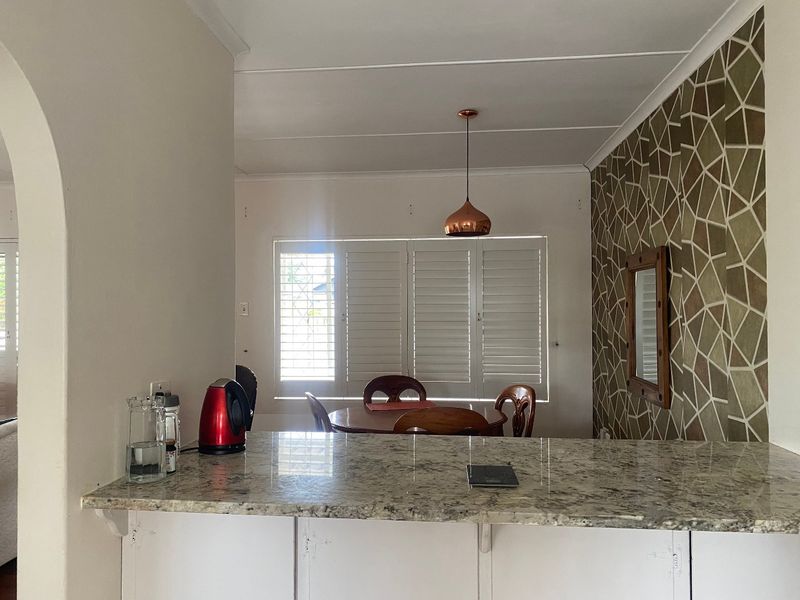 Open plan kitchen and dining area featuring a granite breakfast bar, shutter blinds, and a decorative feature wall.