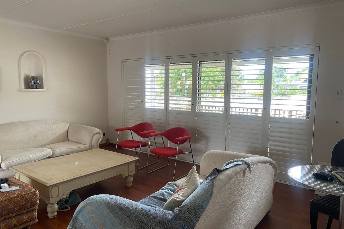 Spacious living room featuring warm hardwood flooring, a decorative recessed wall niche, and large white plantation shutters providing natural light and privacy.