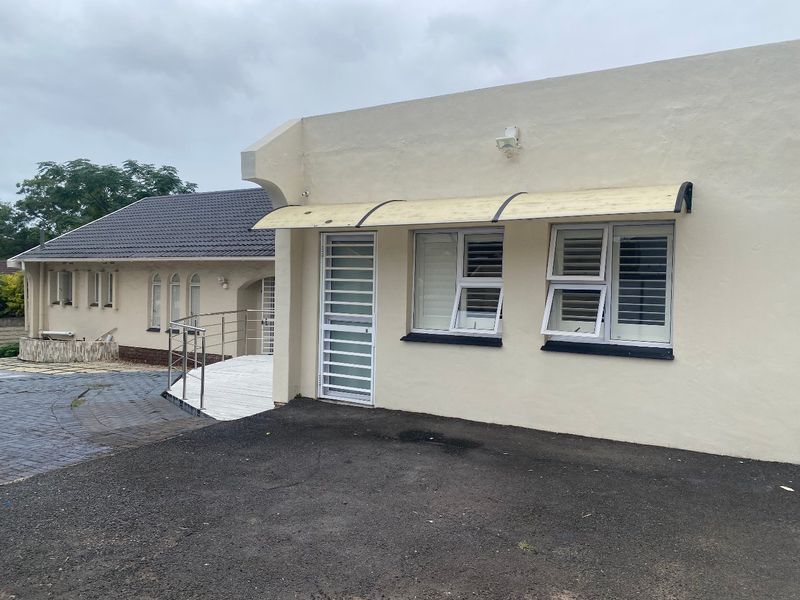 Exterior view of the property featuring a paved driveway, security gate, and window shutters with a protective awning.