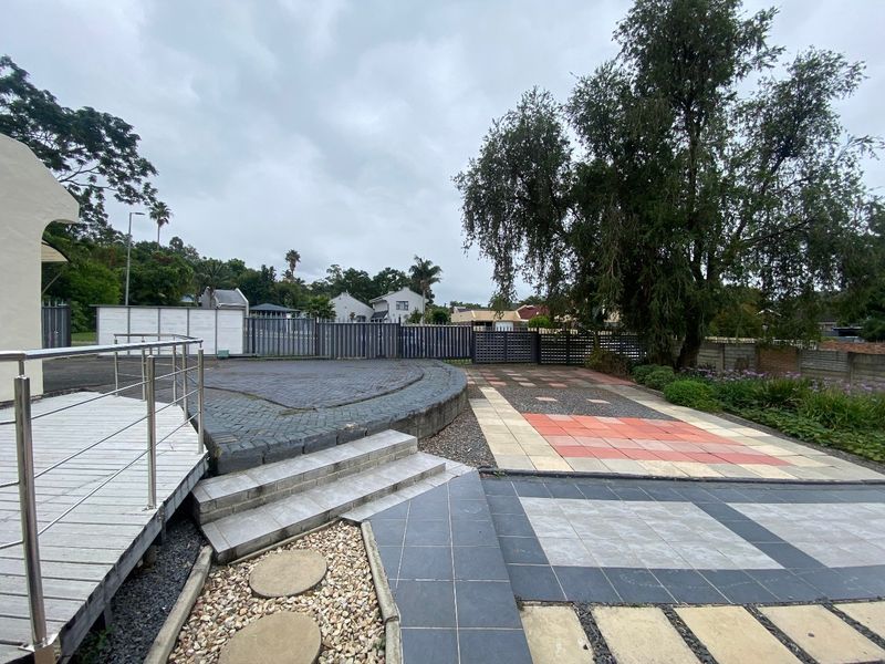 A spacious rear outdoor area featuring a raised deck with stainless steel railings, paved patio sections, and established garden landscaping.
