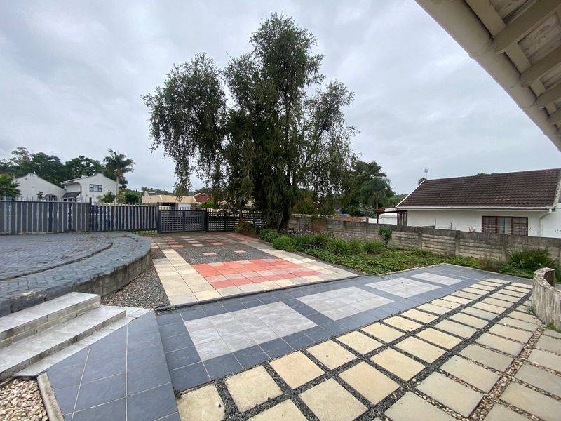 A spacious rear garden area featuring multi-textured paved sections, a retaining wall, and secure boundary fencing, offering potential for outdoor entertainment.