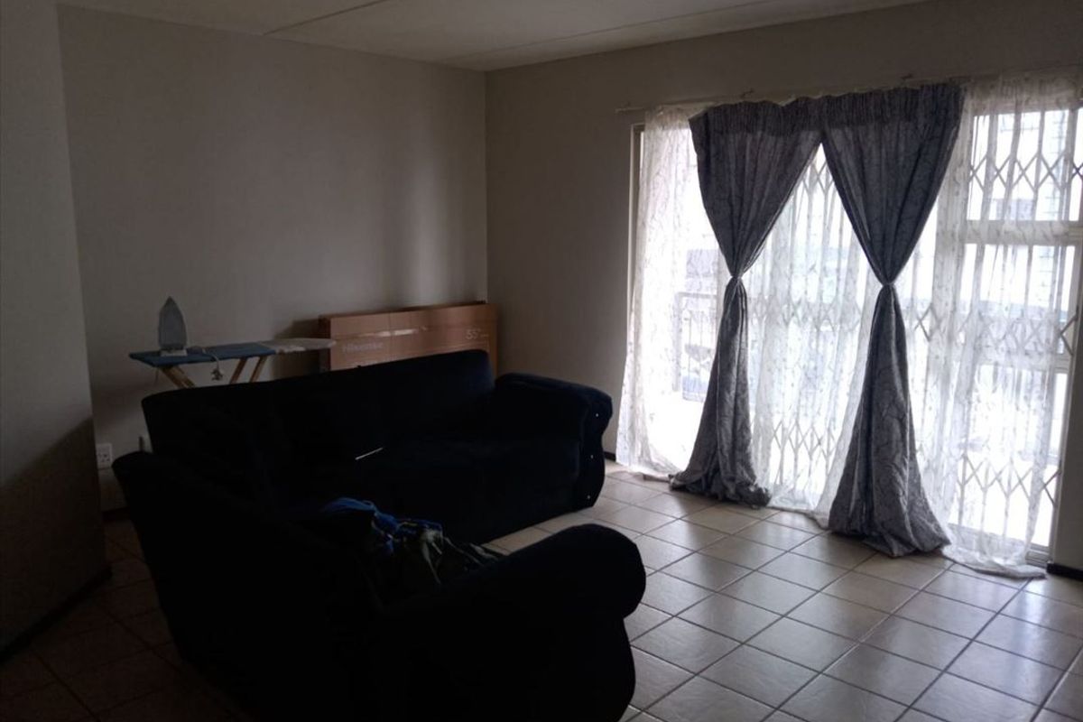 A living room featuring tiled flooring and a sliding door with an integrated security gate, providing access to the exterior.