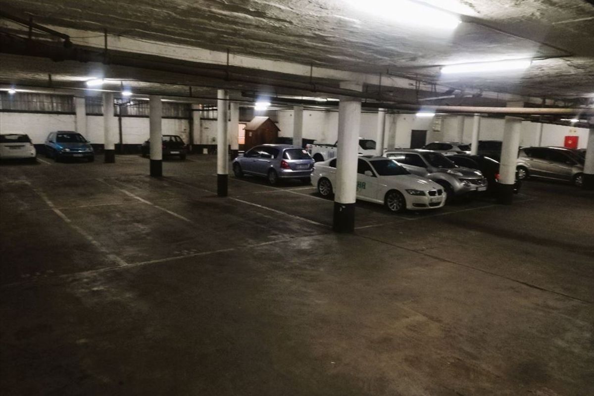 A large underground parking garage featuring concrete columns, fluorescent lighting, and marked parking bays.