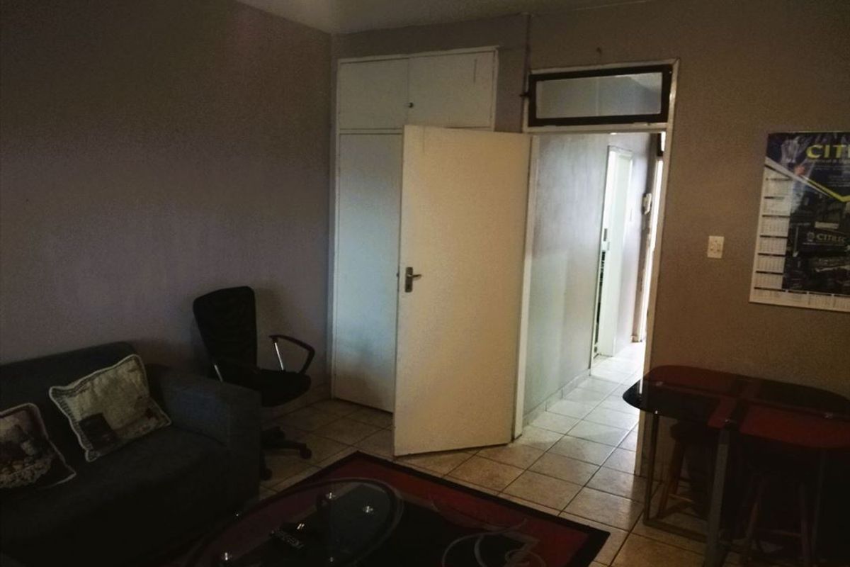 A living room area featuring tiled flooring and a built-in cupboard, providing access to an adjacent hallway.