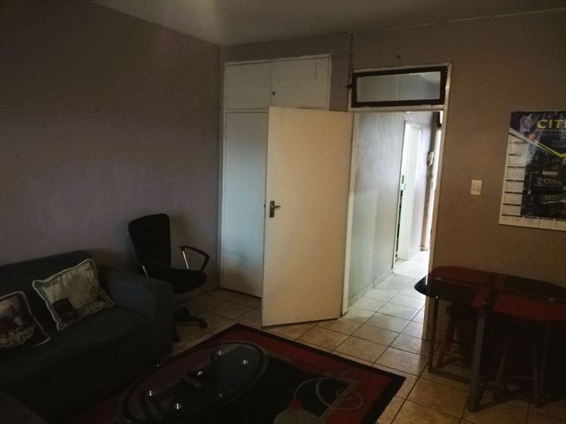 A living room area featuring tiled flooring and a built-in cupboard, providing access to an adjacent hallway.