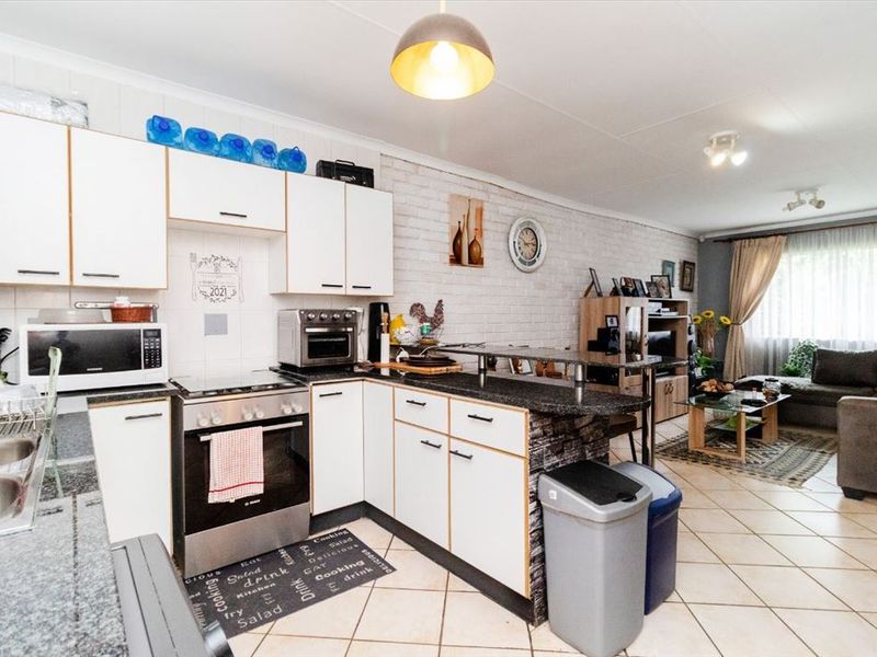 Open-plan living area featuring a kitchen with white cabinetry, granite countertops, breakfast bar, and an adjacent lounge space with tiled flooring.