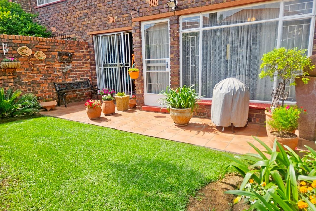 A private rear garden featuring a paved patio area, established lawn, and direct access to the townhouse interior through sliding glass doors.