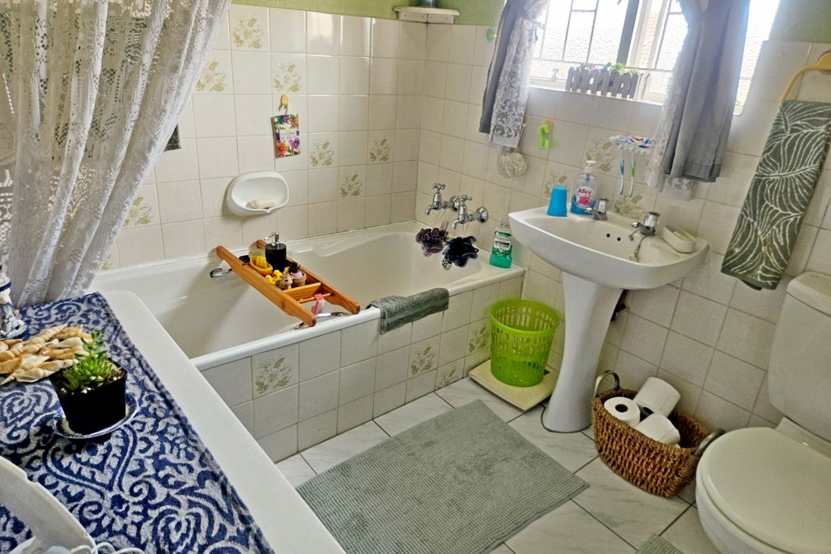 A dated bathroom featuring a standard bathtub, pedestal sink, and toilet with original wall tiling and window security bars.