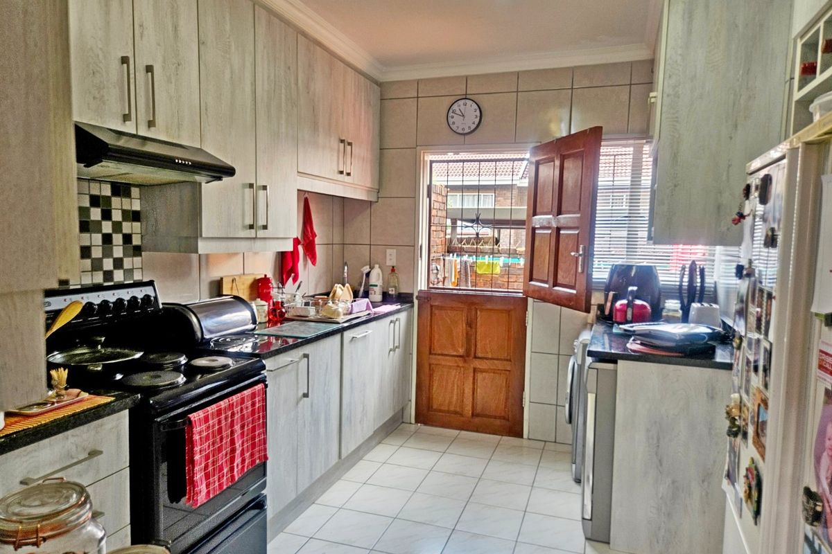 A functional kitchen featuring light wood-grain cabinetry, dark countertops, a built-in extractor fan, and tiled flooring with direct access to the exterior.