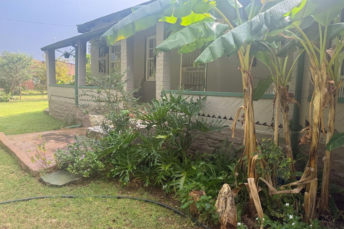 A charming farmhouse exterior featuring a covered veranda with decorative masonry detailing and established garden landscaping.