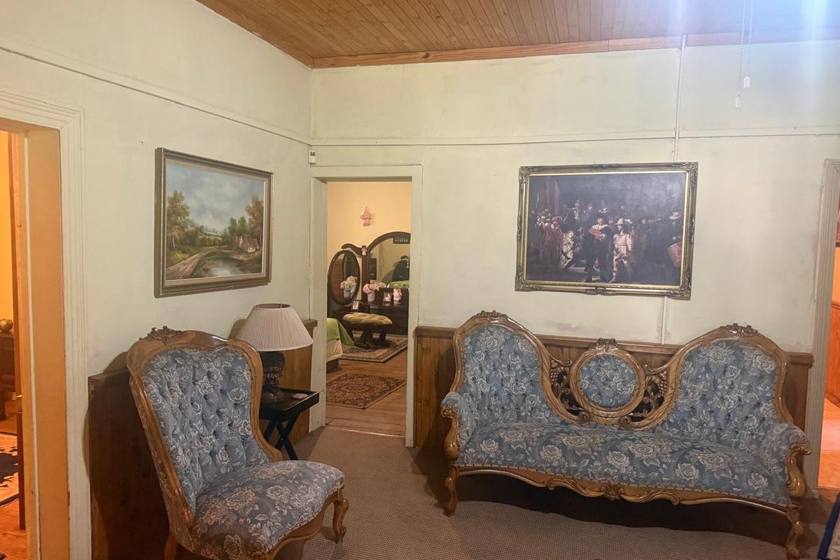A traditional living room featuring timber ceiling paneling, wooden wainscoting, and carpeted flooring, providing a classic, dated aesthetic.