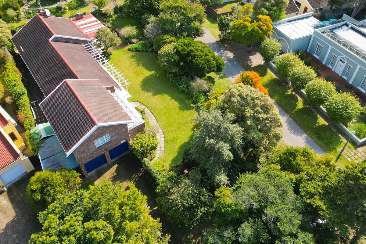Aerial view of the property showcasing the tiled roof, double garage, and expansive landscaped garden with mature trees.