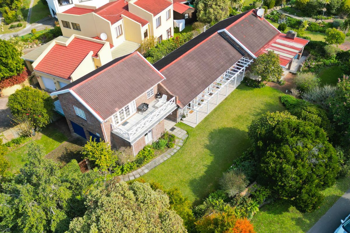 Aerial view of a residential property featuring a multi-level house with a tiled roof, balcony, covered patio, and a spacious landscaped garden.