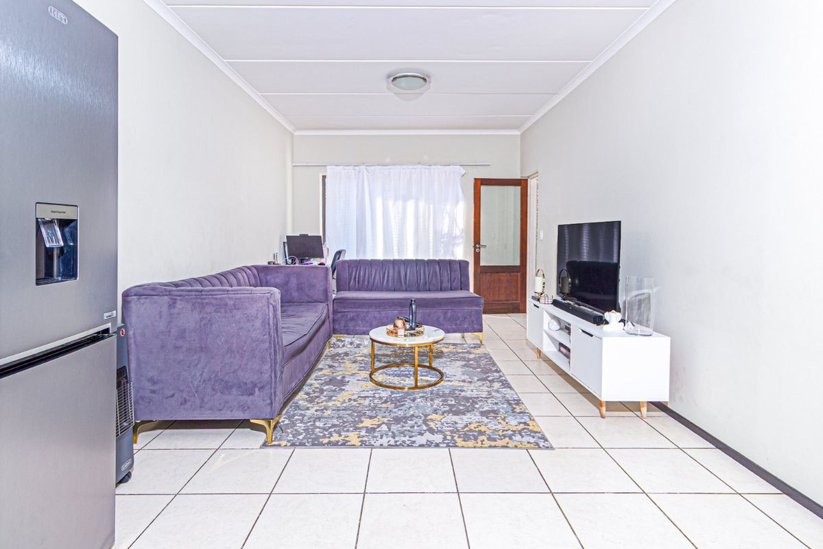 A bright living room featuring white tiled flooring, coved ceilings, and a classic timber door with glass inserts.