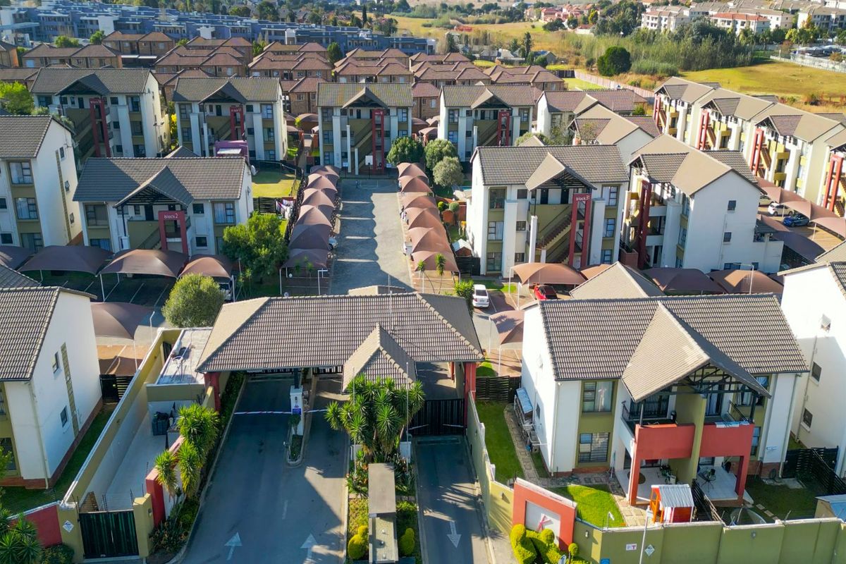 Aerial view of a residential apartment complex featuring a secure gated entrance, paved driveways, and multiple multi-story apartment blocks with carports.