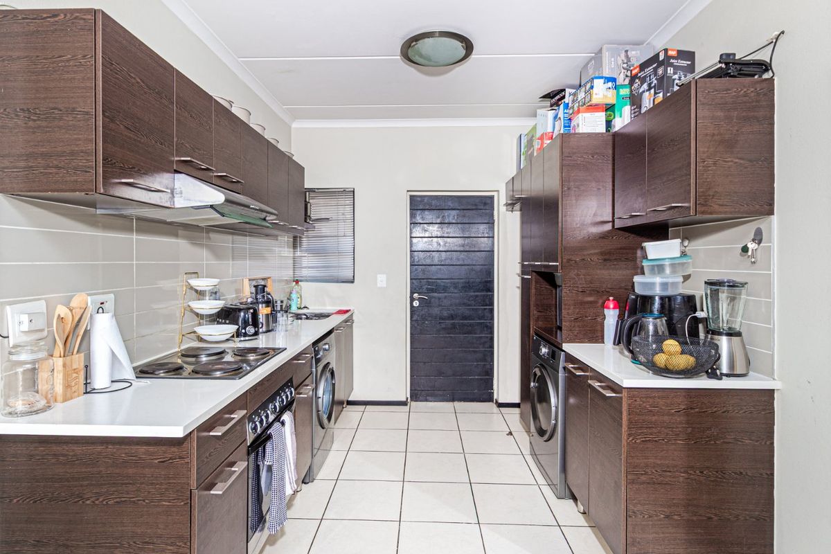 A functional galley-style kitchen featuring dark wood cabinetry, white countertops, tiled flooring, and integrated appliances including a hob, oven, and washing machine.