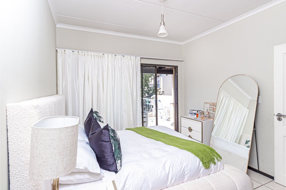 A bright bedroom featuring tiled flooring, neutral walls, and a sliding glass door providing access to an outdoor area.