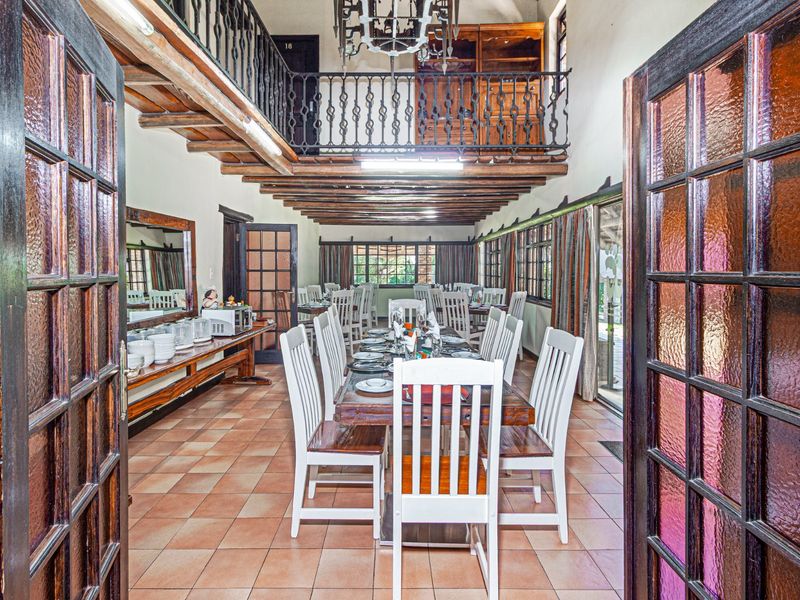 Spacious dining room featuring exposed timber ceiling beams, terracotta flooring, and a mezzanine level with wrought iron railings, creating a rustic commercial atmosphere.