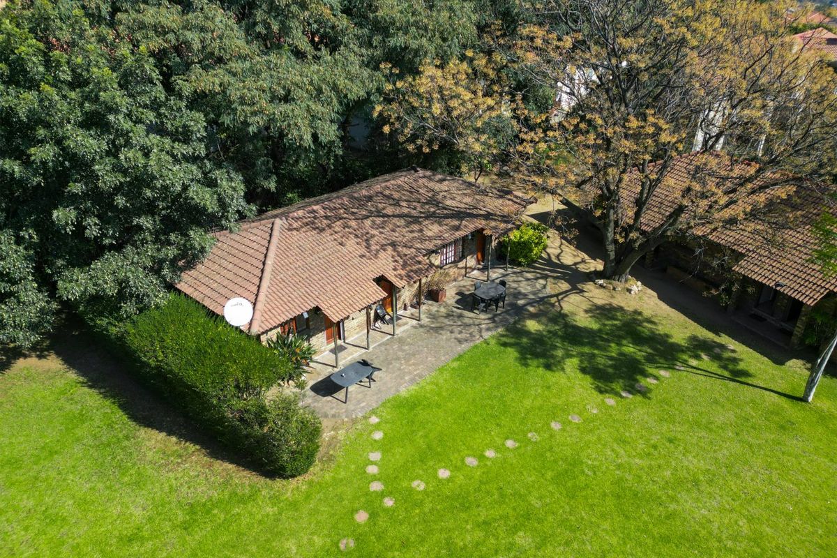 Aerial view of a commercial property featuring a tiled roof building, a paved patio area, and a well-maintained garden with mature trees.