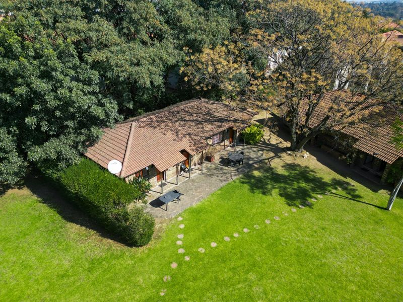 Aerial view of a commercial property featuring a tiled roof building, a paved patio area, and a well-maintained garden with mature trees.