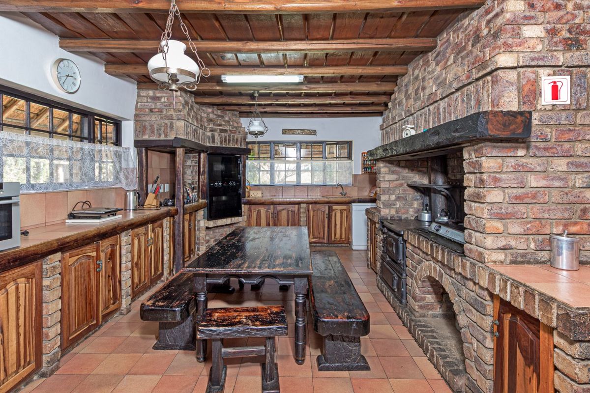 Rustic kitchen featuring exposed timber beam ceilings, brick masonry walls, built-in brick fireplace, and traditional wooden cabinetry with tiled flooring.