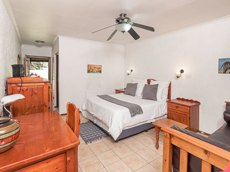 A functional bedroom featuring tiled flooring, a ceiling fan, and wall-mounted lighting, providing a comfortable and practical space.