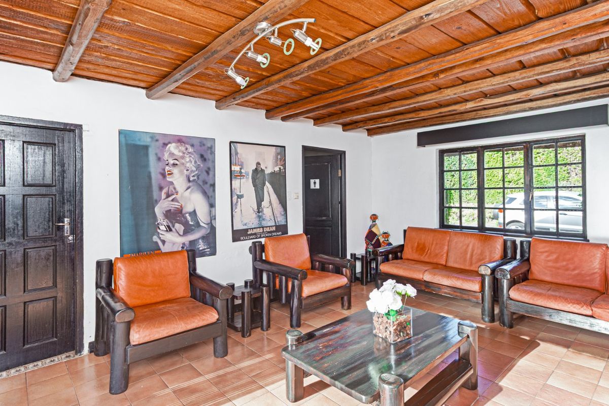 A rustic living area featuring a distinctive exposed timber beam ceiling, ceramic tiled flooring, and large multi-pane windows providing natural light.