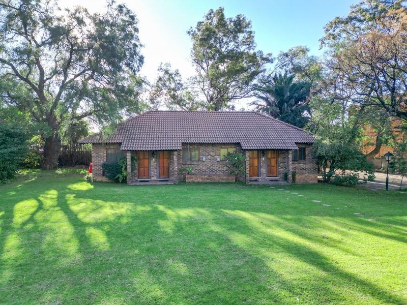 A well-maintained single-story commercial building featuring a face brick exterior, tiled roof, and multiple private entrances set within a spacious, landscaped garden.