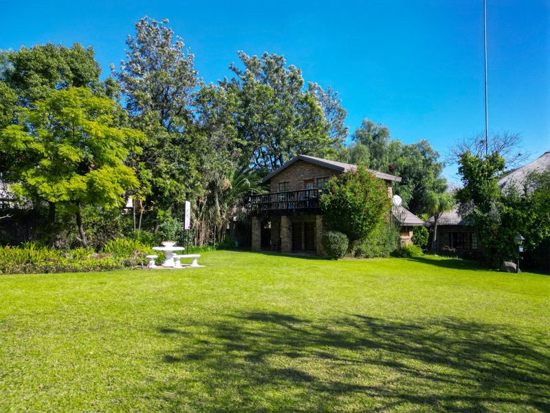 A view of the rear exterior of the brick building, featuring a balcony and a well-maintained, expansive green garden with mature trees.