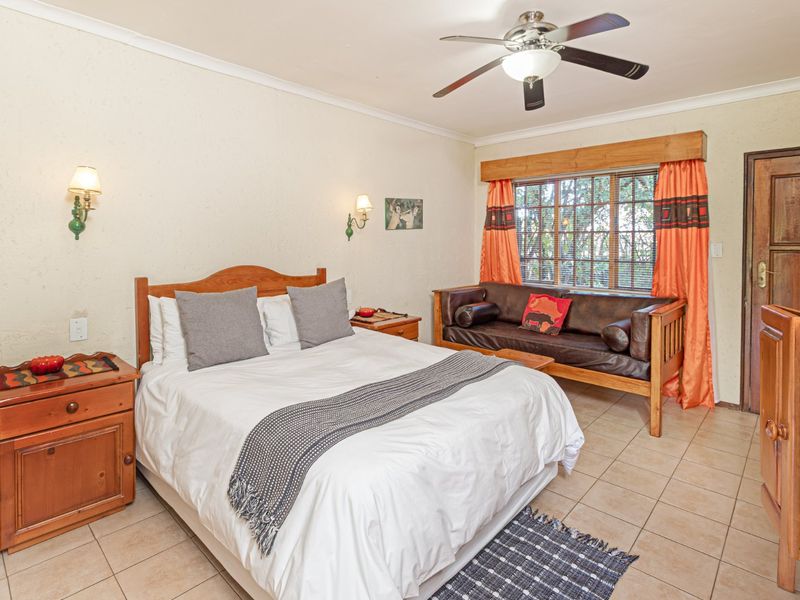 A bedroom featuring tiled flooring, a ceiling fan, wall sconces, and a wooden window frame with views of the exterior.