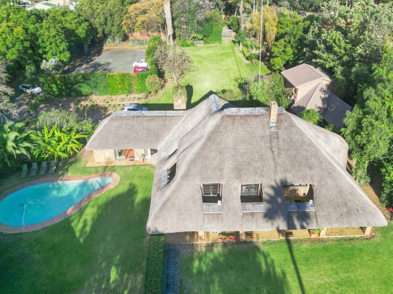 Aerial view of a property featuring a large thatched roof building, a swimming pool, and extensive landscaped garden grounds.