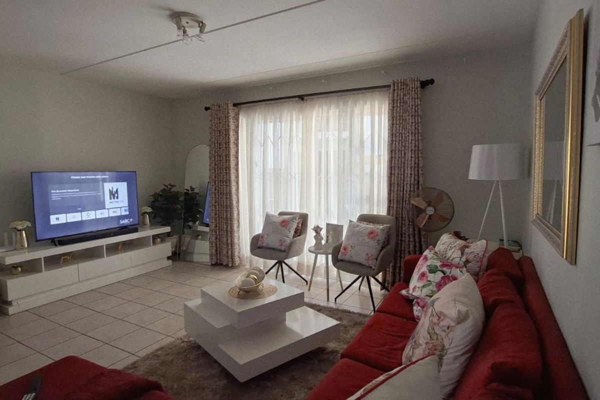 A comfortable living room featuring tiled flooring and large windows with curtain rails, providing natural light and access to the exterior.