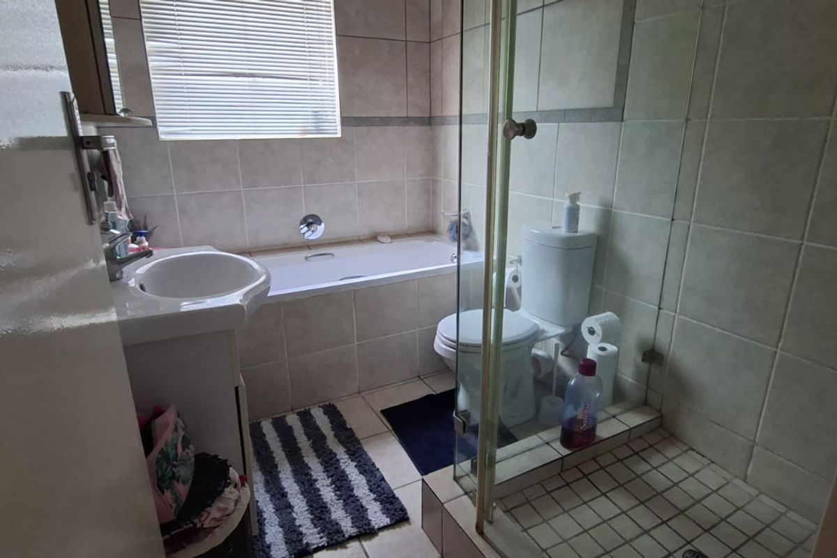 A functional bathroom featuring a bathtub, separate glass-enclosed shower, pedestal basin, and toilet with neutral wall and floor tiling.