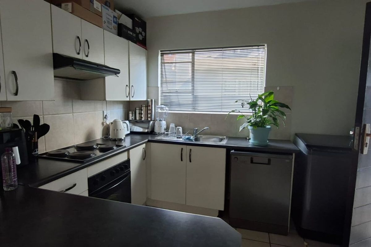 A functional kitchen featuring white cabinetry, dark countertops, an electric hob, built-in oven, and a stainless steel sink with a window view.