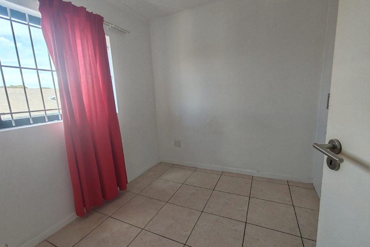 A vacant bedroom featuring tiled flooring, a window with security bars, and neutral wall finishes, offering a blank canvas for personalization.