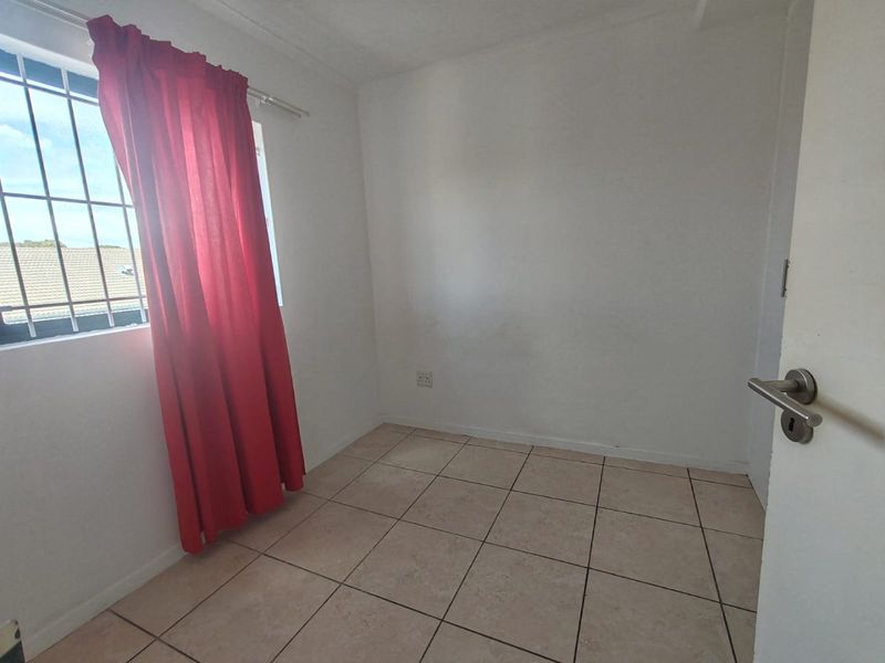 A vacant bedroom featuring tiled flooring, a window with security bars, and neutral wall finishes, offering a blank canvas for personalization.