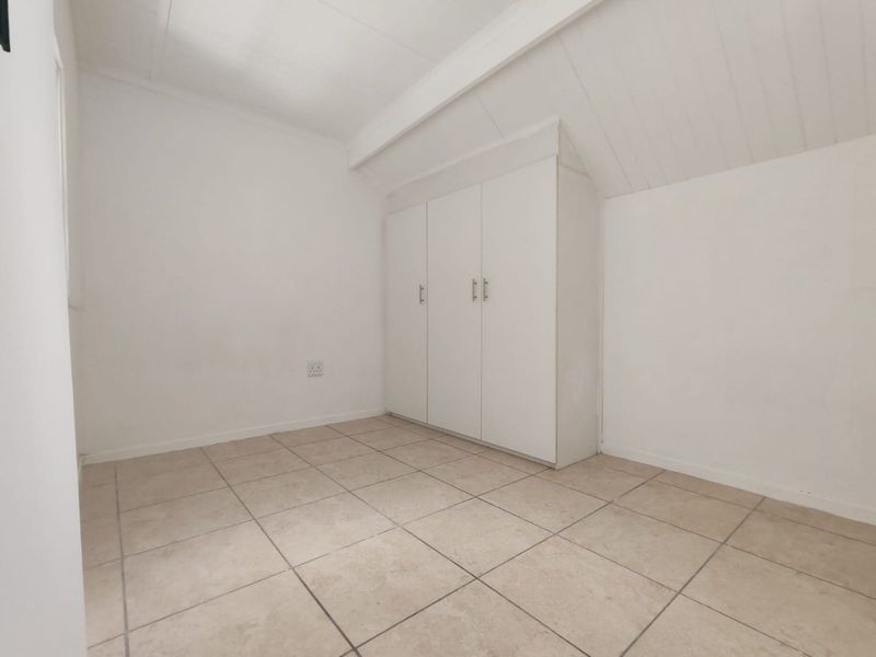 An empty bedroom featuring tiled flooring, a sloped ceiling, and built-in cupboards.
