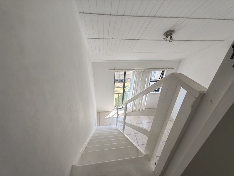 A view looking down a staircase with white painted railings, tiled flooring, and a tongue and groove ceiling leading to a ground floor area.